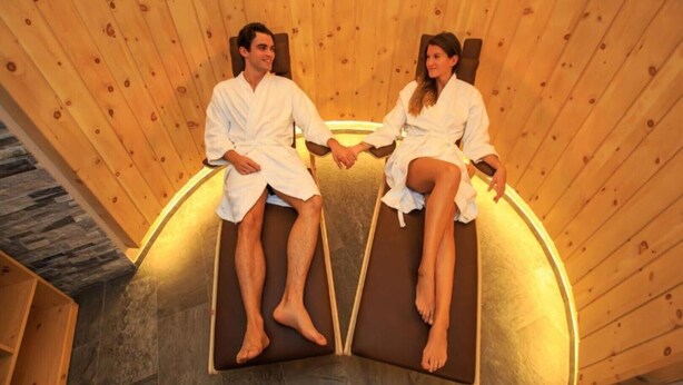 Dos personas sentadas en una sauna con paredes de madera y suelo de piedra.