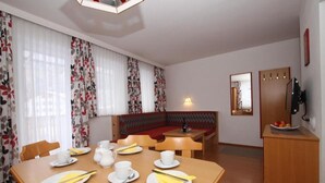 Un comedor con una mesa de madera dispuesta para dos personas, un banco con cojín rojo y un televisor sobre un mueble de madera.