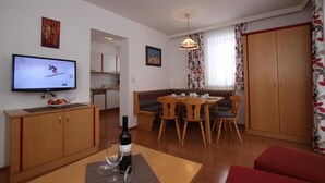 Un espacio habitable compacto con comedor, kitchenette y televisor mostrando un evento deportivo.
