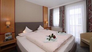 Habitación de hotel con una cama grande, dos mesitas de noche, una silla y un ventanal con cortinas.