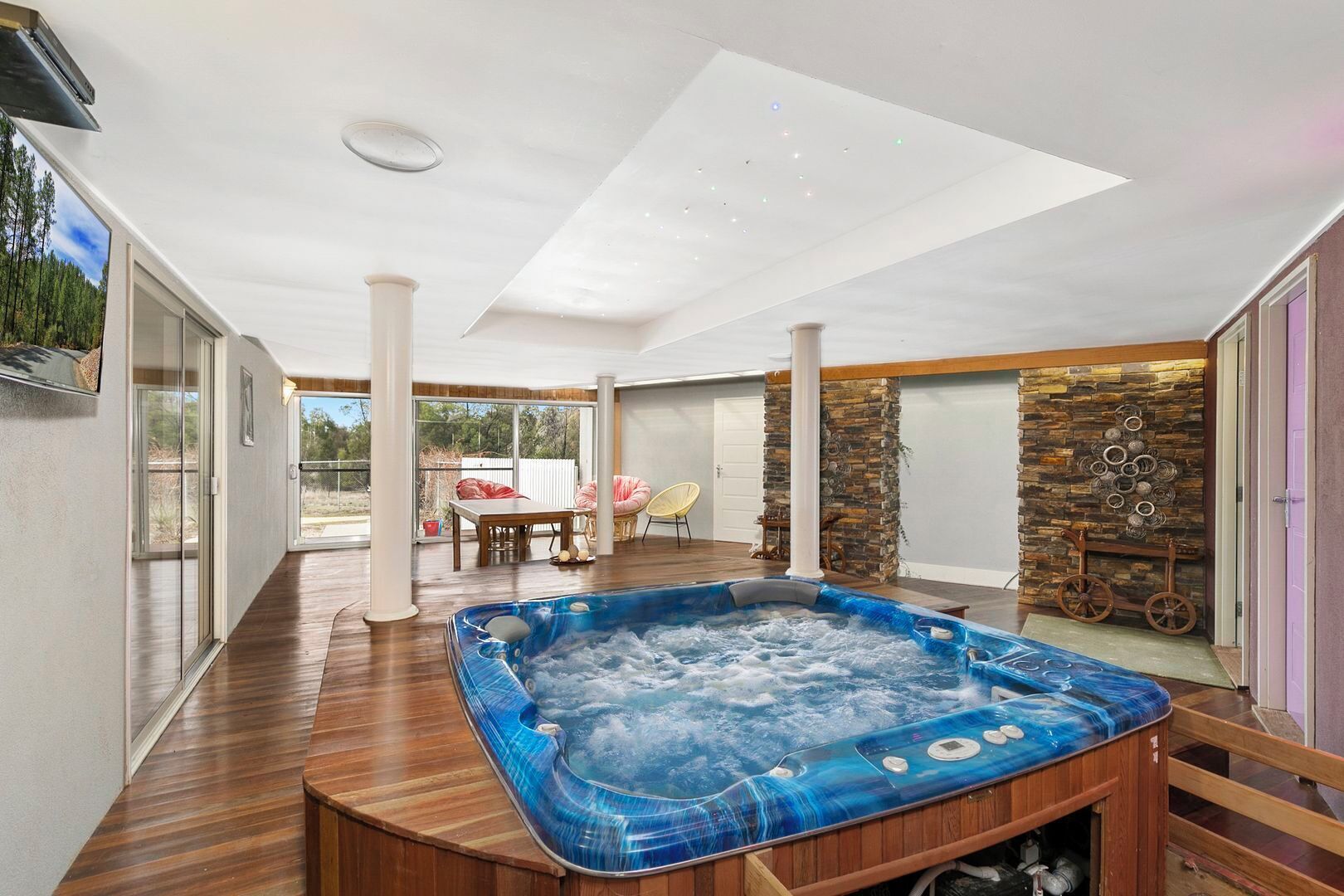 Ein modernes Hallenbad mit Holzterrasse, Steinwand und Glastür zum Außenbereich.