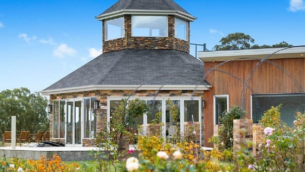 Una casa moderna con una torre de piedra, un porche cubierto y un jardín lleno de flores.