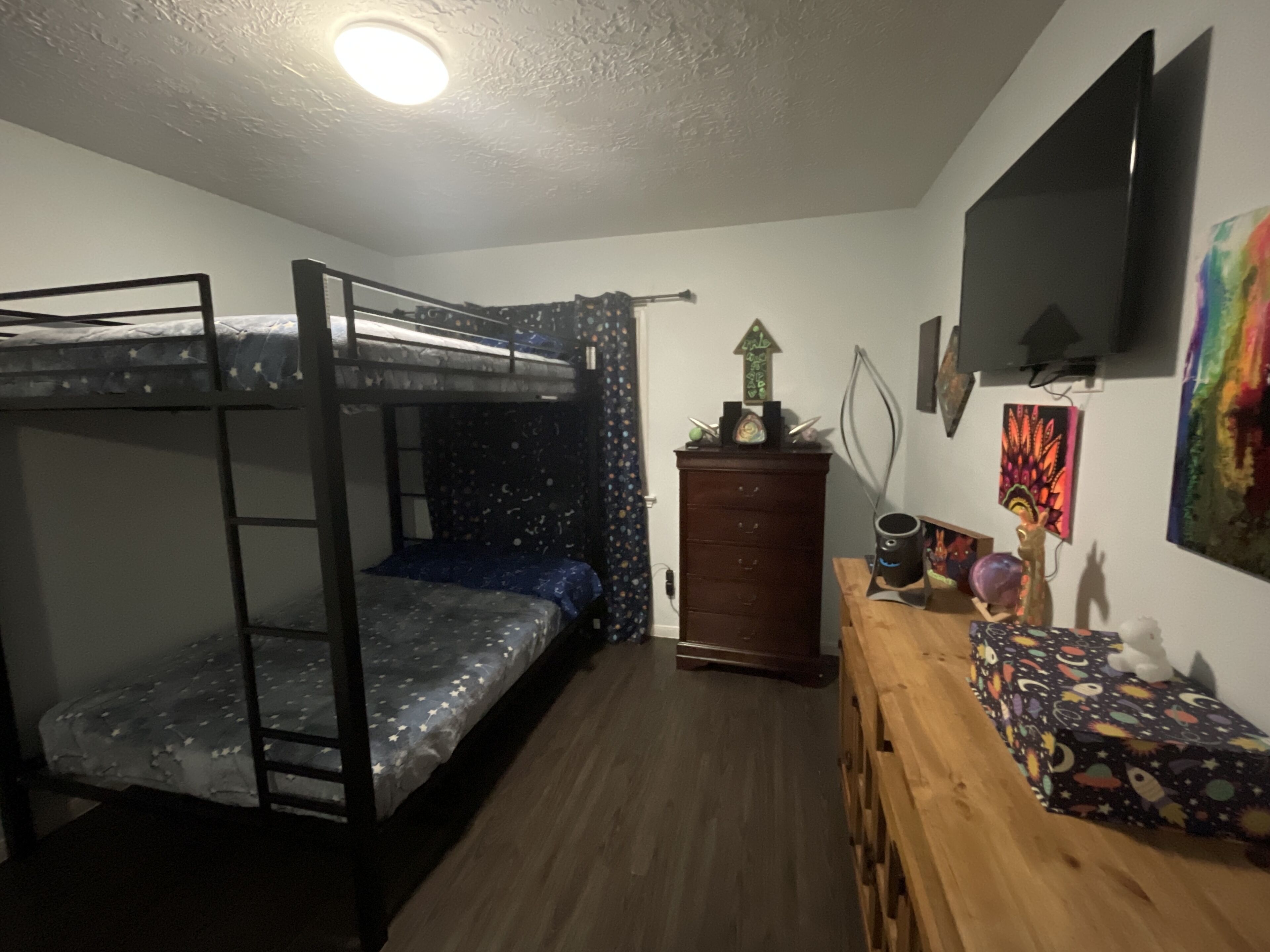 Une chambre avec un lit superposé, une commode, un bureau et un téléviseur fixé au mur.