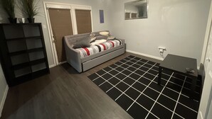 Ein Zimmer mit grauem Sofa, Deckenventilator, schwarz-weiß gefliestem Boden und einer Tür mit Spiegel darüber.
