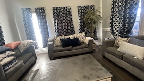 Ein Wohnzimmer mit zwei Sofas, einem Couchtisch und gemusterten Vorhängen.