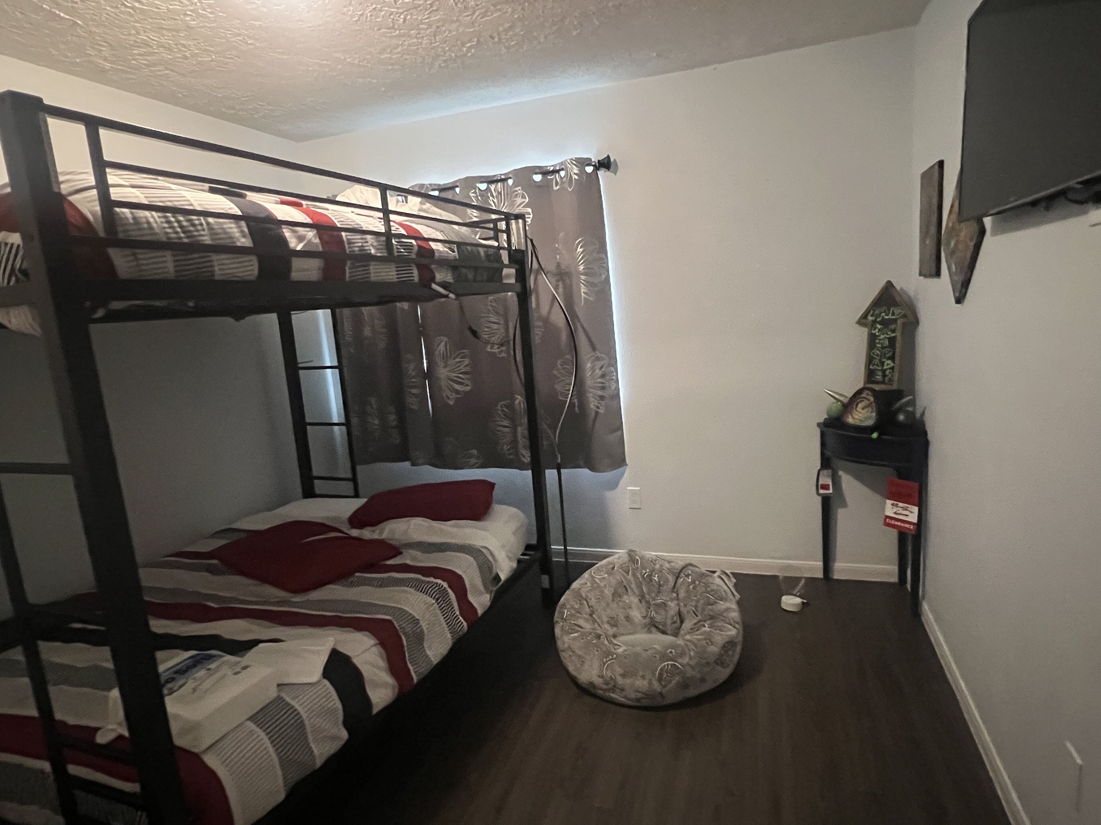 A bunk bed with a patterned bedspread, a round pet bed, a small shelf with decorative items, and a wall-mounted TV.