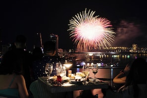 A table with food and drinks, a city skyline, and fireworks in the background.