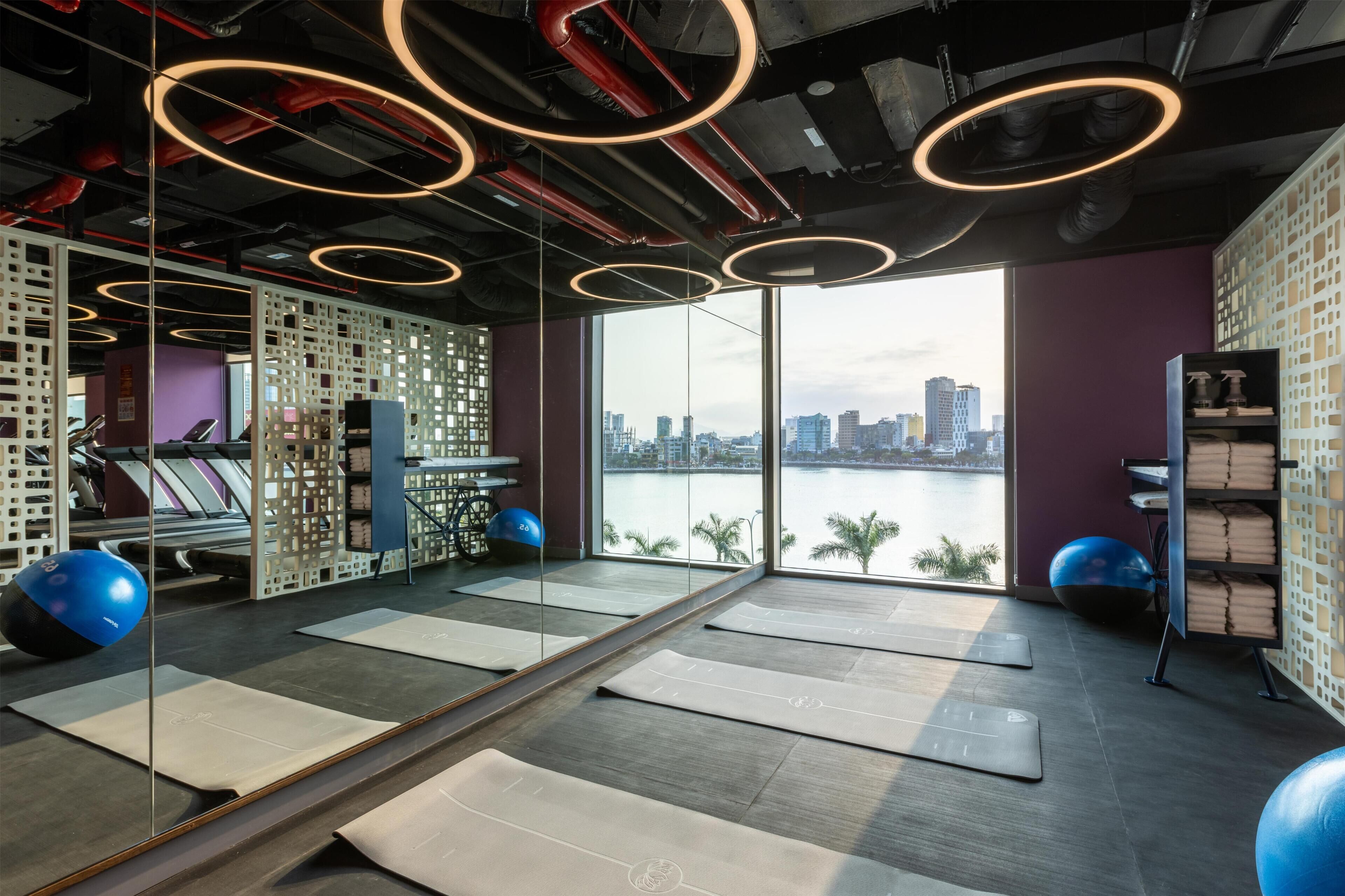 A gym with exercise mats, exercise balls, and a view of a cityscape through large windows.