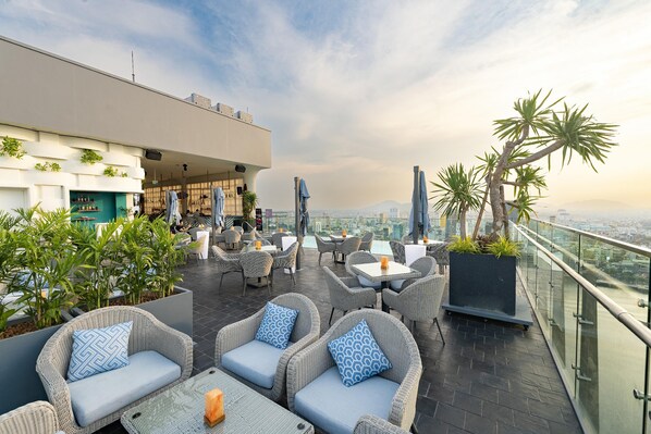 A rooftop terrace with wicker furniture, a bar area, and a view of the cityscape. - Wink Danang Riverside, Unscripted by Hyatt - 24 Hours stay (Da Nang)