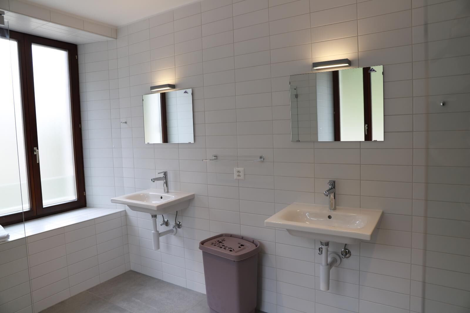 Une salle de bain avec deux lavabos, une fenêtre et une poubelle.