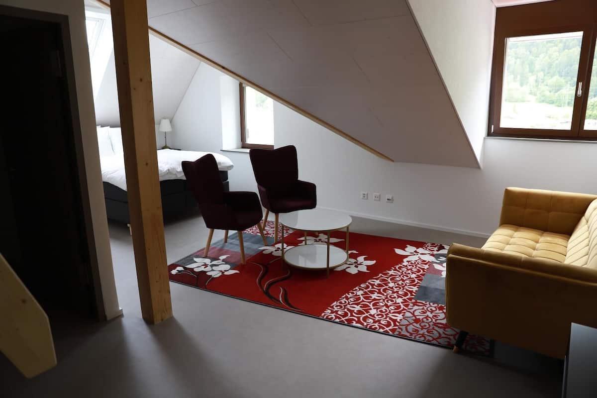 Een moderne kamer met een tapijt met een rood-wit patroon, een gele bank en twee donkere stoelen rond een kleine witte tafel.