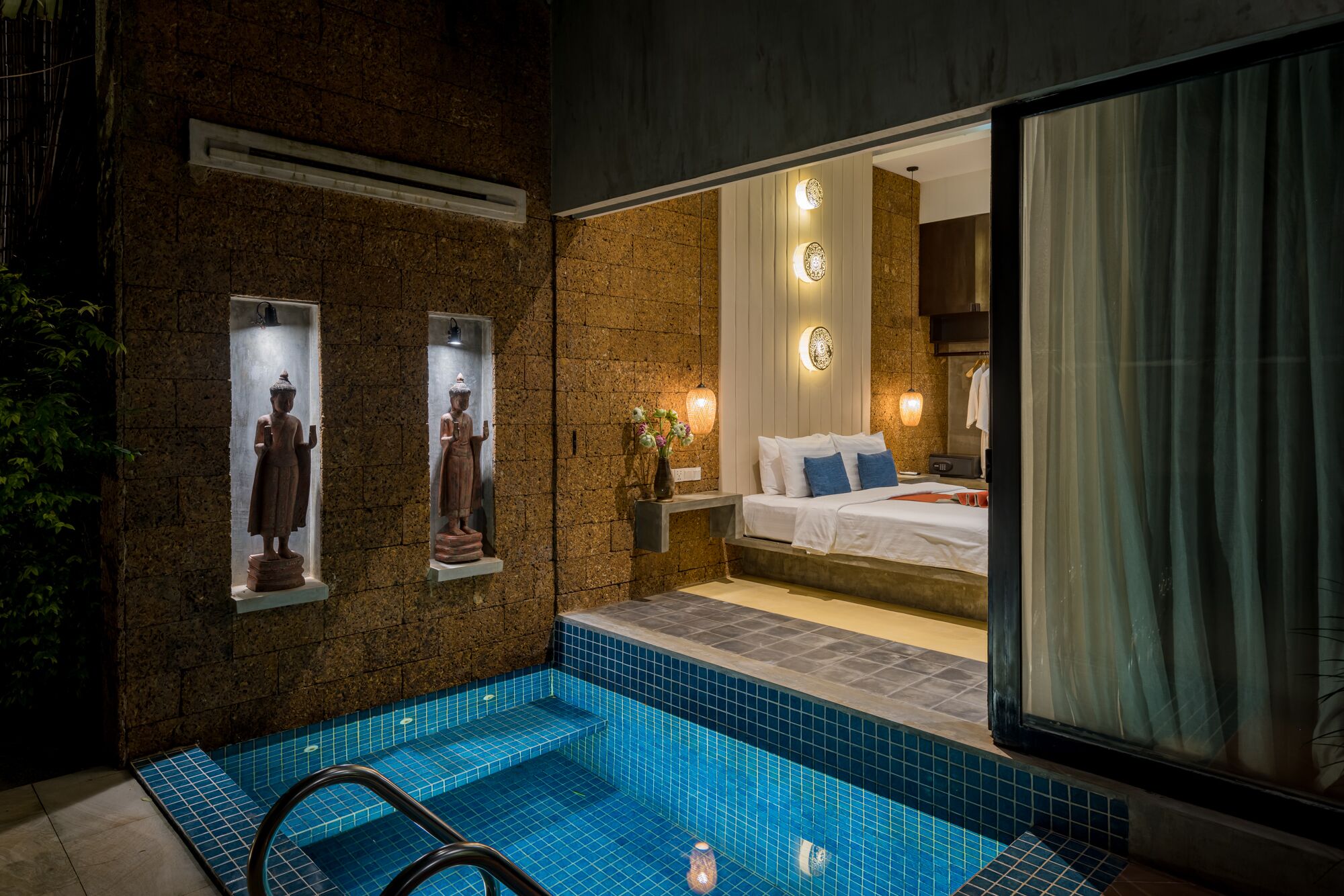 A modern hotel room with a large window, a small pool, and two statues on the wall.