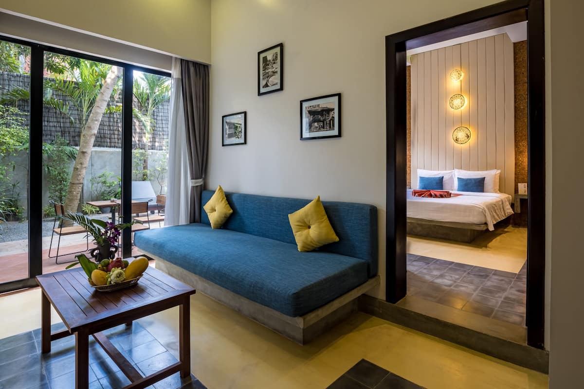A modern room with a blue sofa, a wooden table with fruit, and a bed with a white mattress and blue pillows.