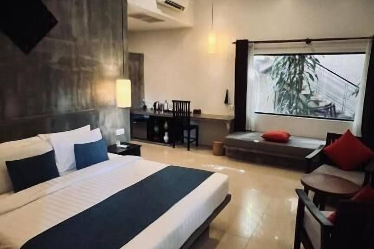 A modern hotel room with a large bed, a desk, a chair, a ceiling fan, and a large window with a city view.