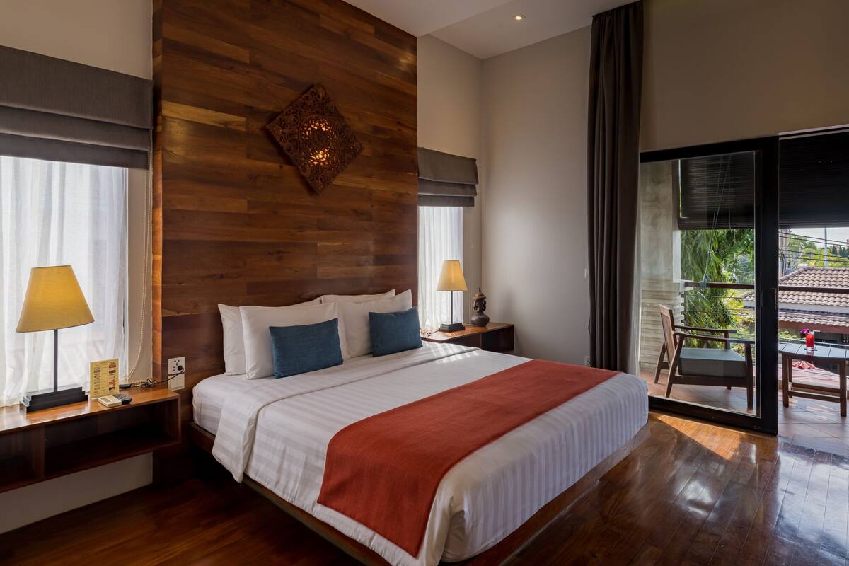 A spacious bedroom with a large bed, wooden headboard, and a view of a balcony.