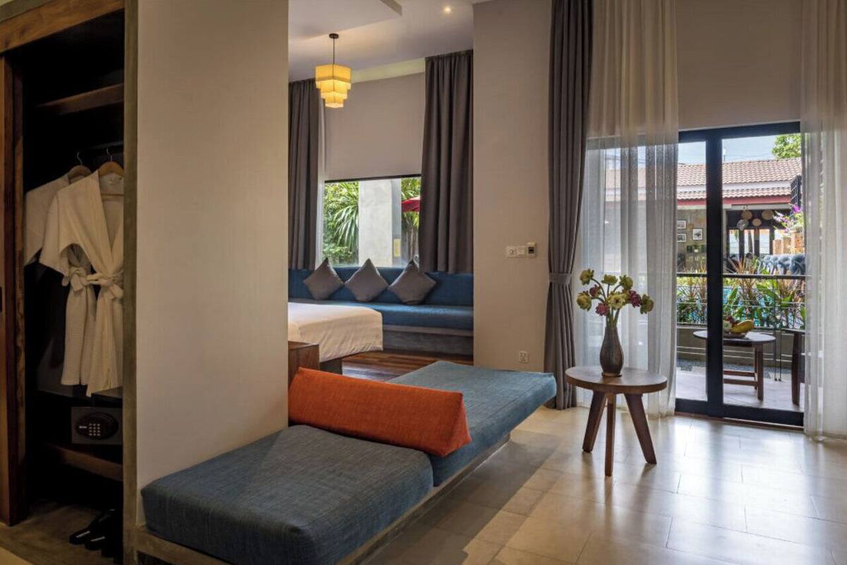 A modern hotel room with a sofa bed, a small table with a vase, and a view of the outside.