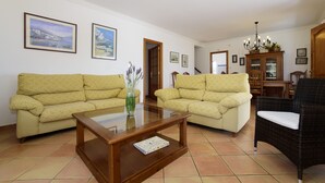 Ein Wohnzimmer mit zwei Sofas, einem Couchtisch, einem Korbstuhl und einer Kommode mit gerahmten Bildern.