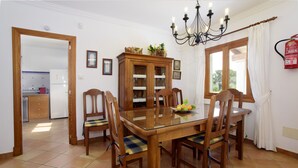 Ein Essbereich mit einem Glastisch, Holzstühlen, einem Holzschrank mit Glastüren und einer Kronleuchter.
