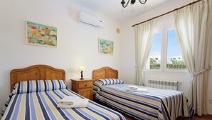Ein Schlafzimmer mit zwei Betten, einem Nachttisch, einer Lampe und einem Fenster mit Vorhängen.