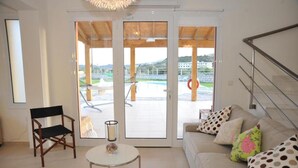 Een woonkamer met een bank, een stoel, een tafel en uitzicht op een buitenruimte met een zwembad en een gebouw op de achtergrond.