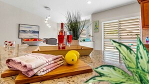 A modern kitchen with a granite countertop, a wooden cutting board, a bowl of fruit, a bottle of red wine, and a potted plant. - Private Pool｜Near Beach｜Fenced Yard｜Outdoor Living (Naples)