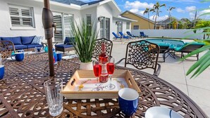 A patio with a table set for two, a pool, and a house in the background. - Private Pool｜Near Beach｜Fenced Yard｜Outdoor Living (Naples)