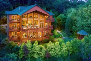 A large, multi-story lodge with balconies and large windows, surrounded by dense forest. - Million $ Views • Hot Tub • Game Room • Sleeps 21 (Gatlinburg)