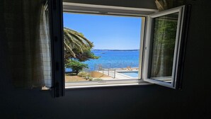 A room with a window overlooking a pool and a clear blue sea.