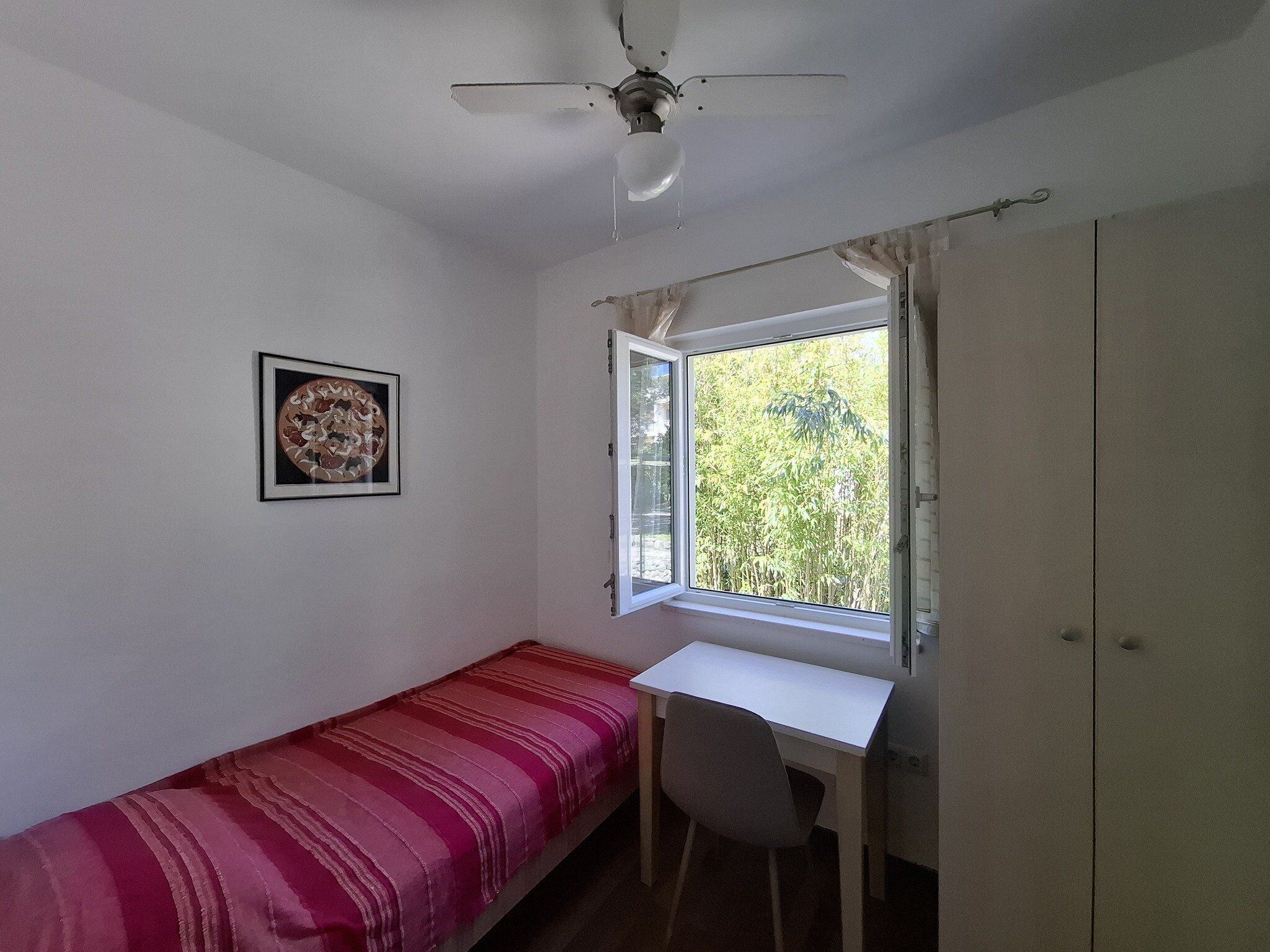 A small room with a single bed, a desk, and a window.