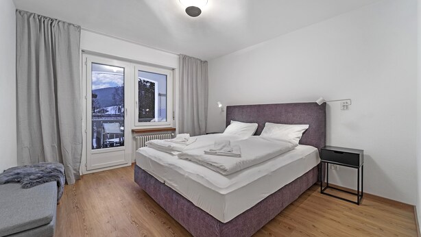 Un dormitorio moderno con una cama grande, una mesita de noche, una ventana con vistas y suelo de madera.