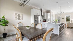 Uma cozinha moderna com armários brancos, uma ilha central com banquetas e uma área de jantar com mesa e cadeiras de madeira.