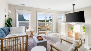 Uma sala de estar moderna com uma televisão grande, um sofá, um espaço de refeições e vista para o exterior.