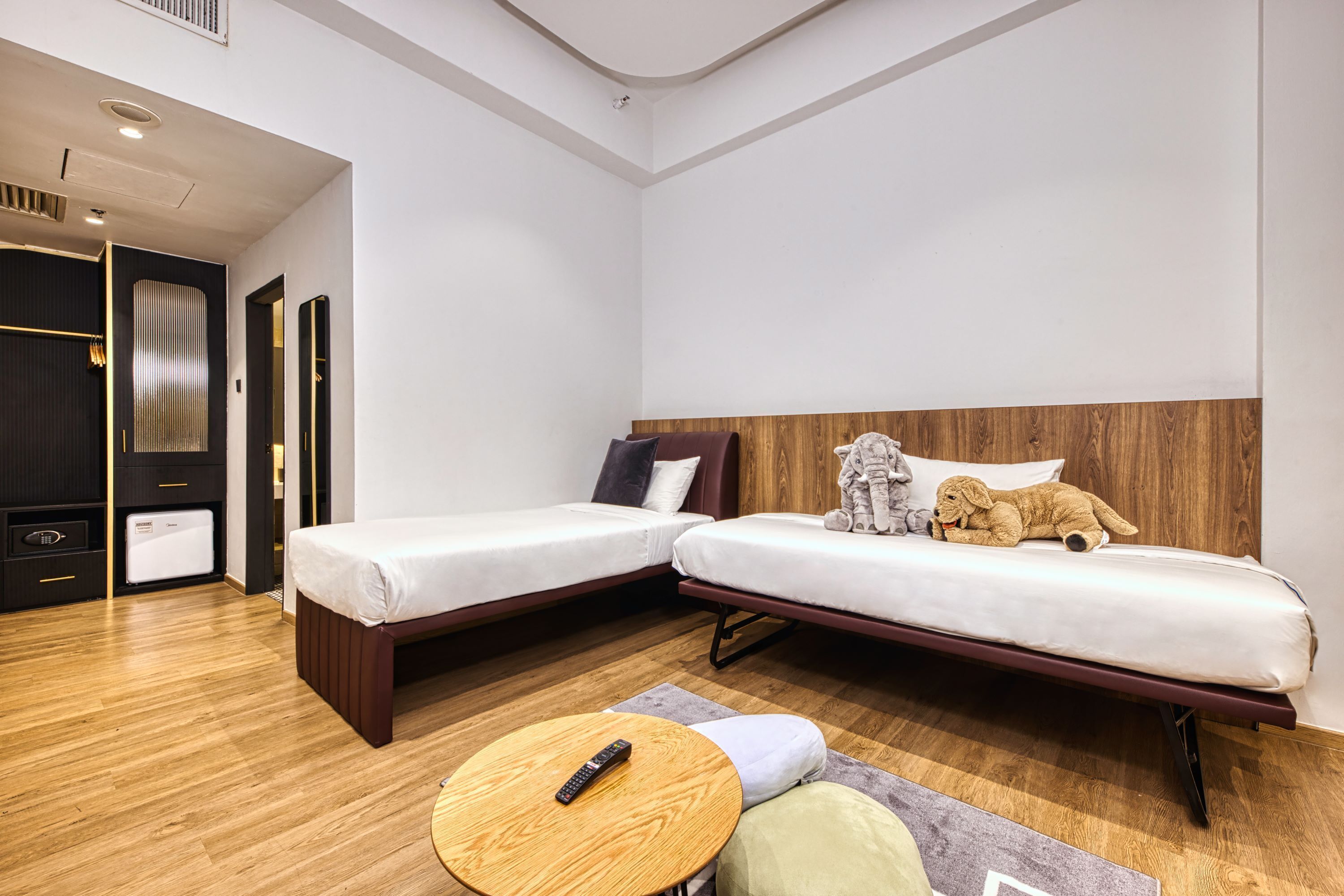 A modern hotel room with two single beds, a wooden floor, a small round table, and a wardrobe.