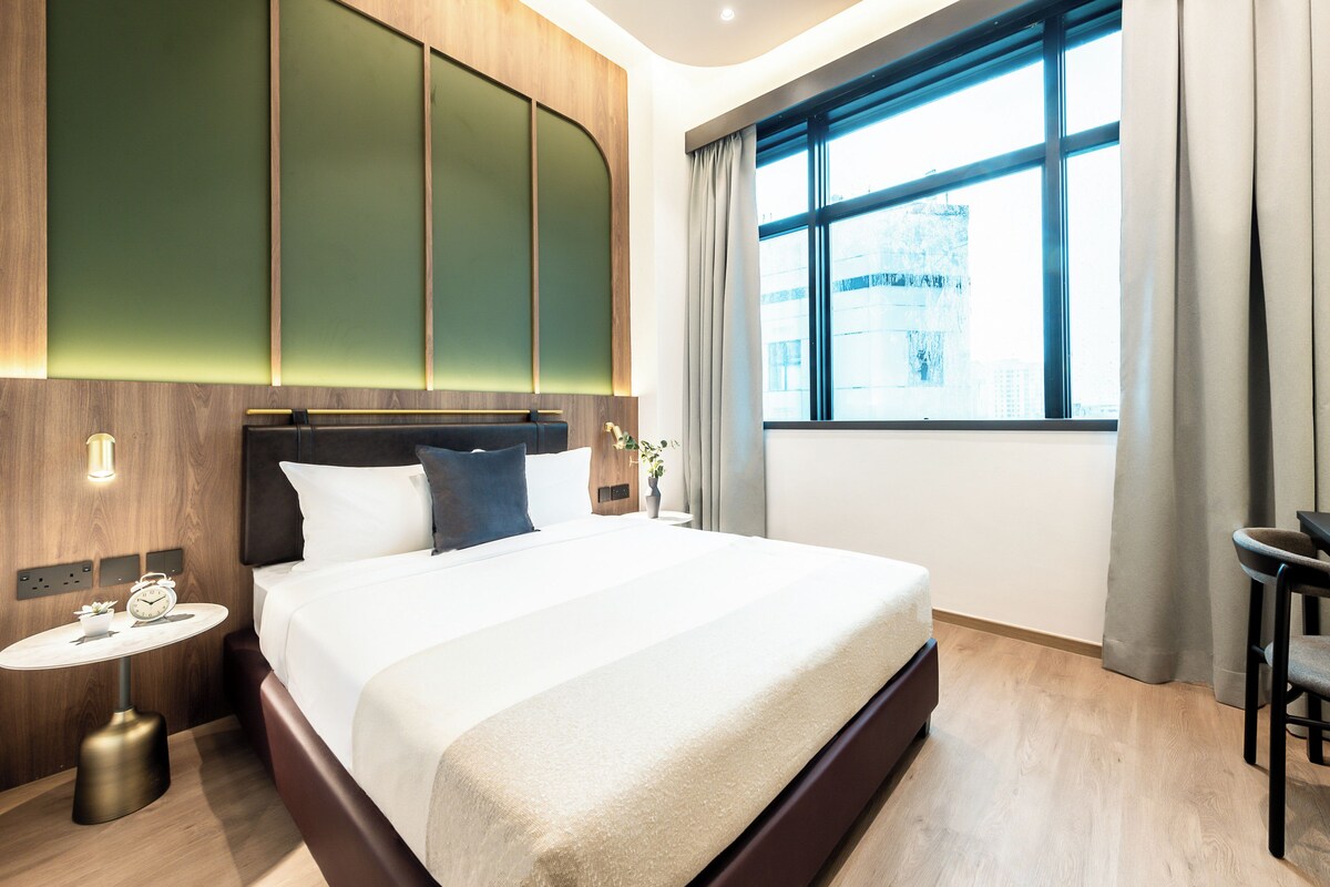 Een moderne hotelkamer met een groot bed, een nachtkastje met een klok en een raam met gordijnen.