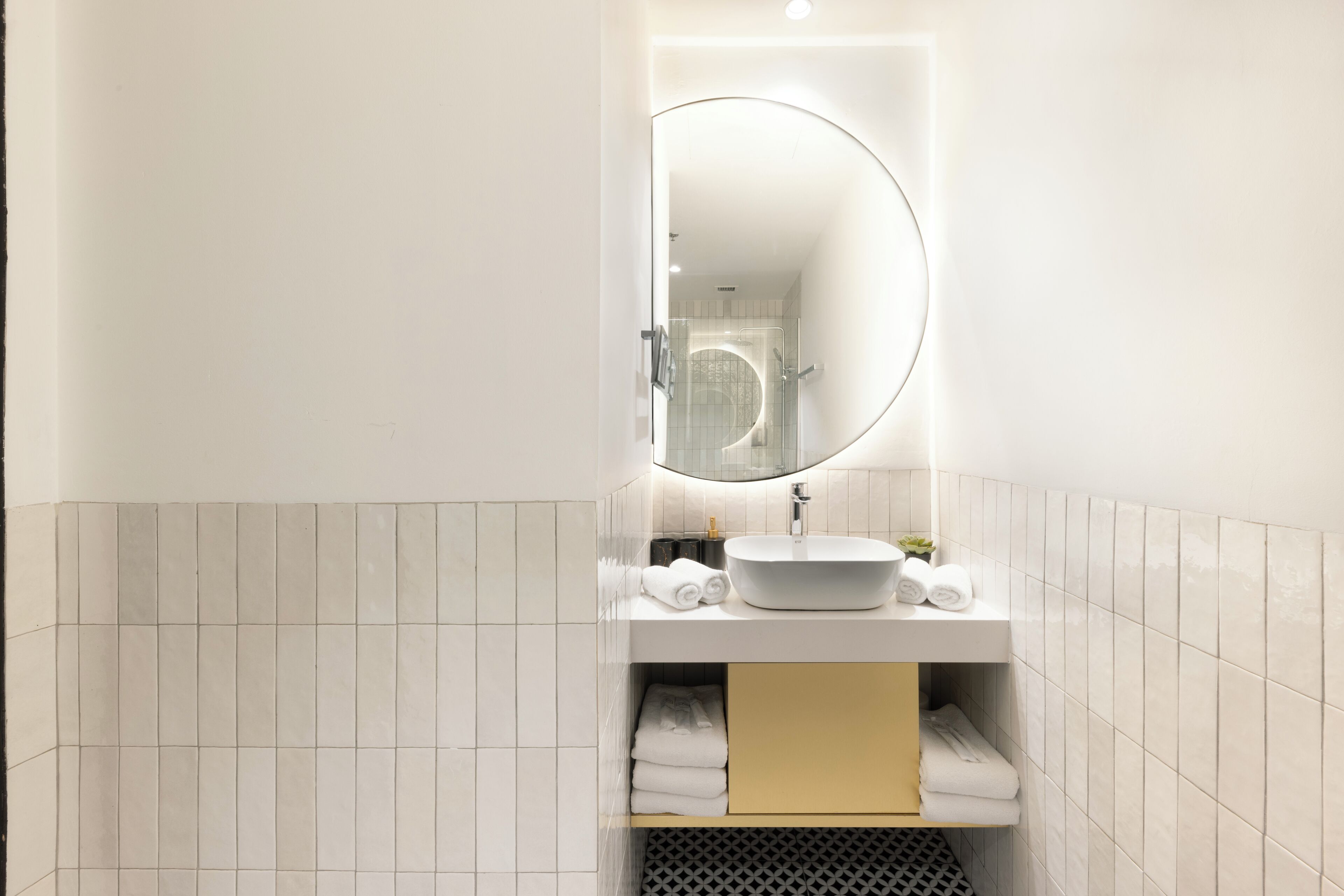 A modern bathroom with a white sink, a round mirror, and a towel rack.