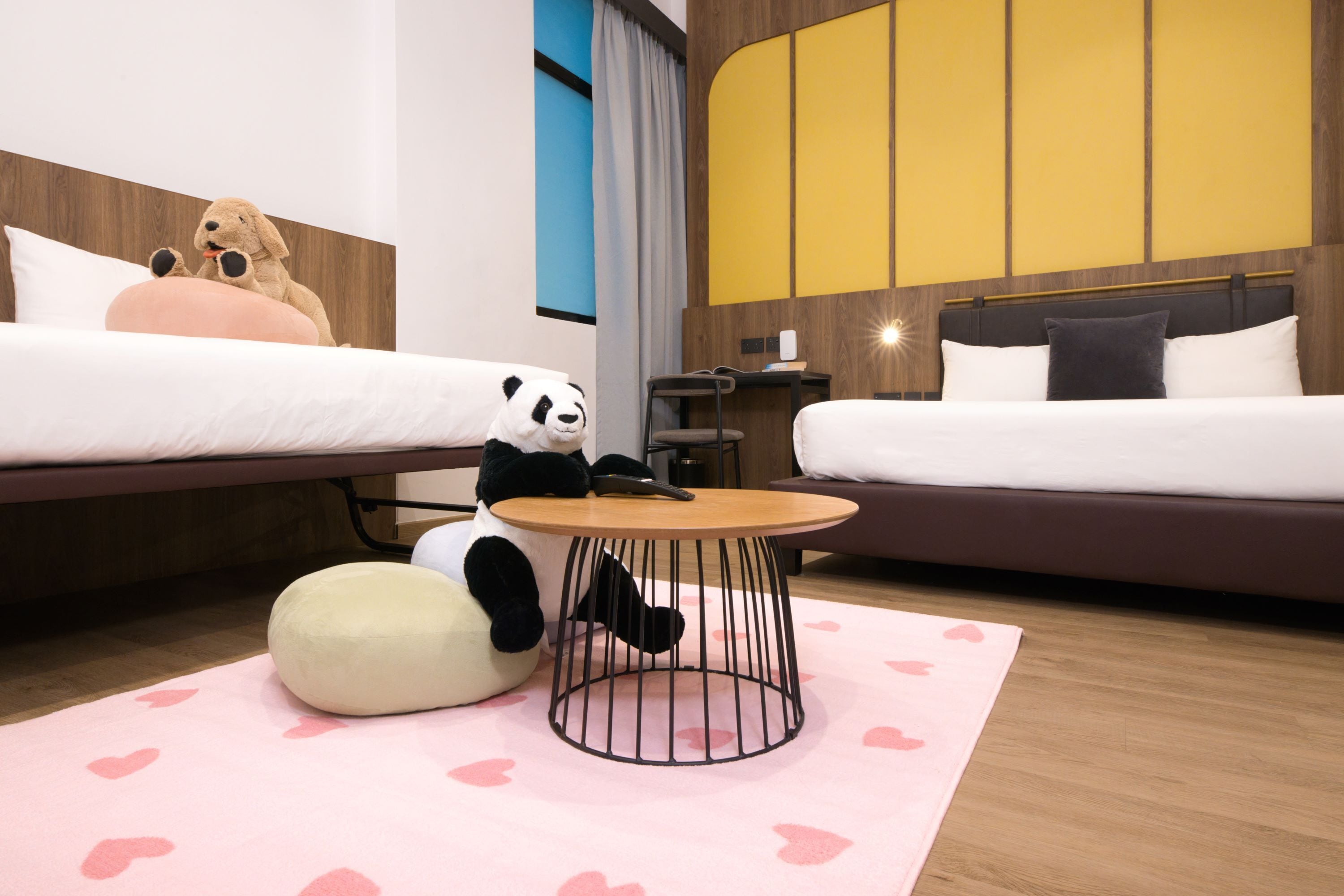 A hotel room with two beds, a round coffee table, and a panda plush toy.