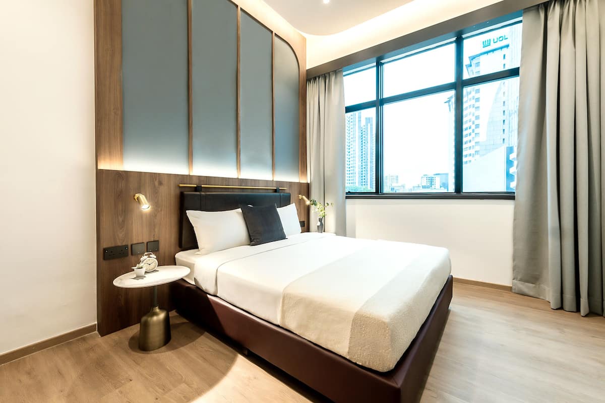 Een moderne hotelkamer met een groot bed, een nachtkastje met een lamp, en uitzicht op de stad door een groot raam.
