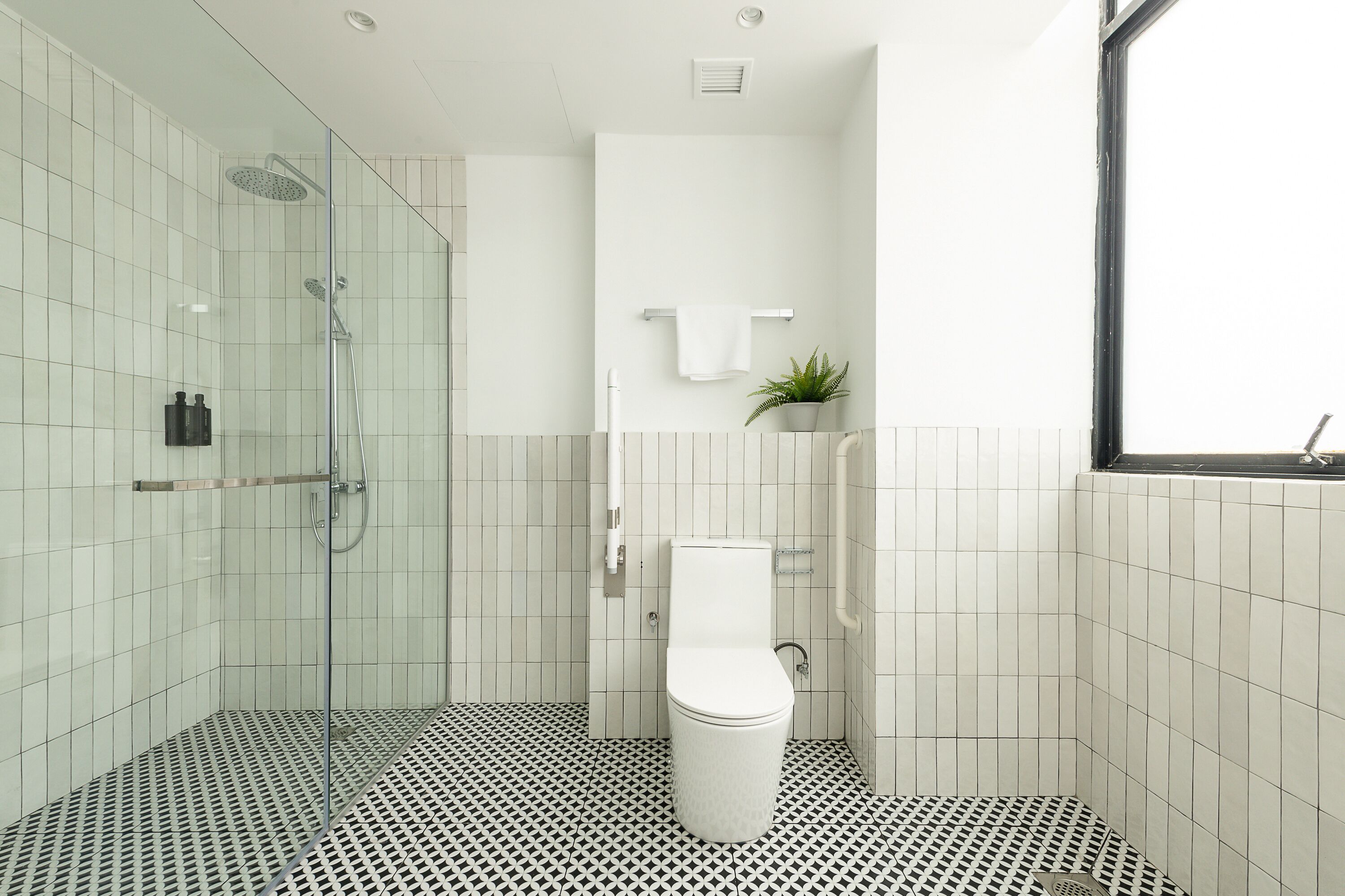 A modern bathroom with a glass-enclosed shower, a white toilet, and a patterned floor.