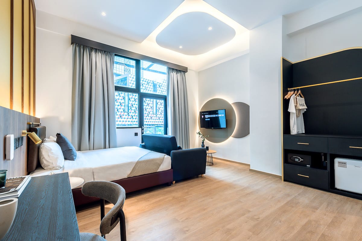 Een moderne hotelkamer met een bed, nachtkastje, stoel, televisie, kledingkast en uitzicht.