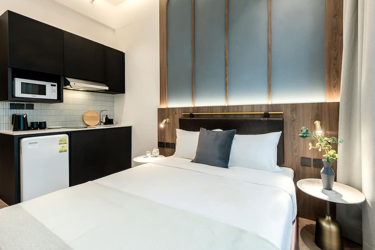 Een moderne hotelkamer met een bed, nachtkastje en een kleine kitchenette.