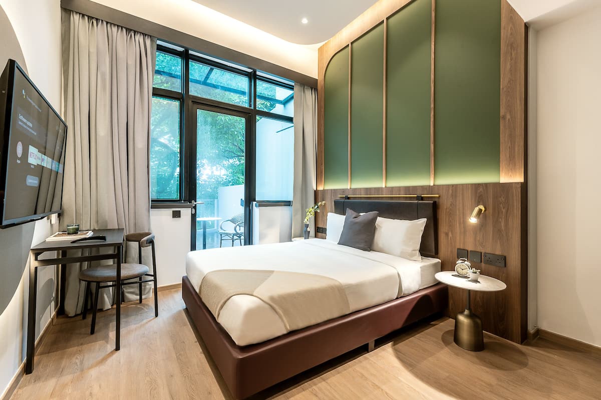 Een moderne hotelkamer met een groot bed, een bureau met stoel, een klein tafeltje met een klok en een televisie aan de muur.