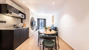 A modern kitchen with built-in appliances, a dining area with a round table and chairs, and a view through a window.