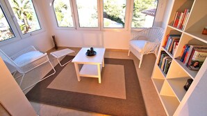 A cozy reading nook with a white wicker chair, a small table, and a bookshelf filled with books. - Charming detached holiday home with private pool–close to beach and fully fenced (Dénia)