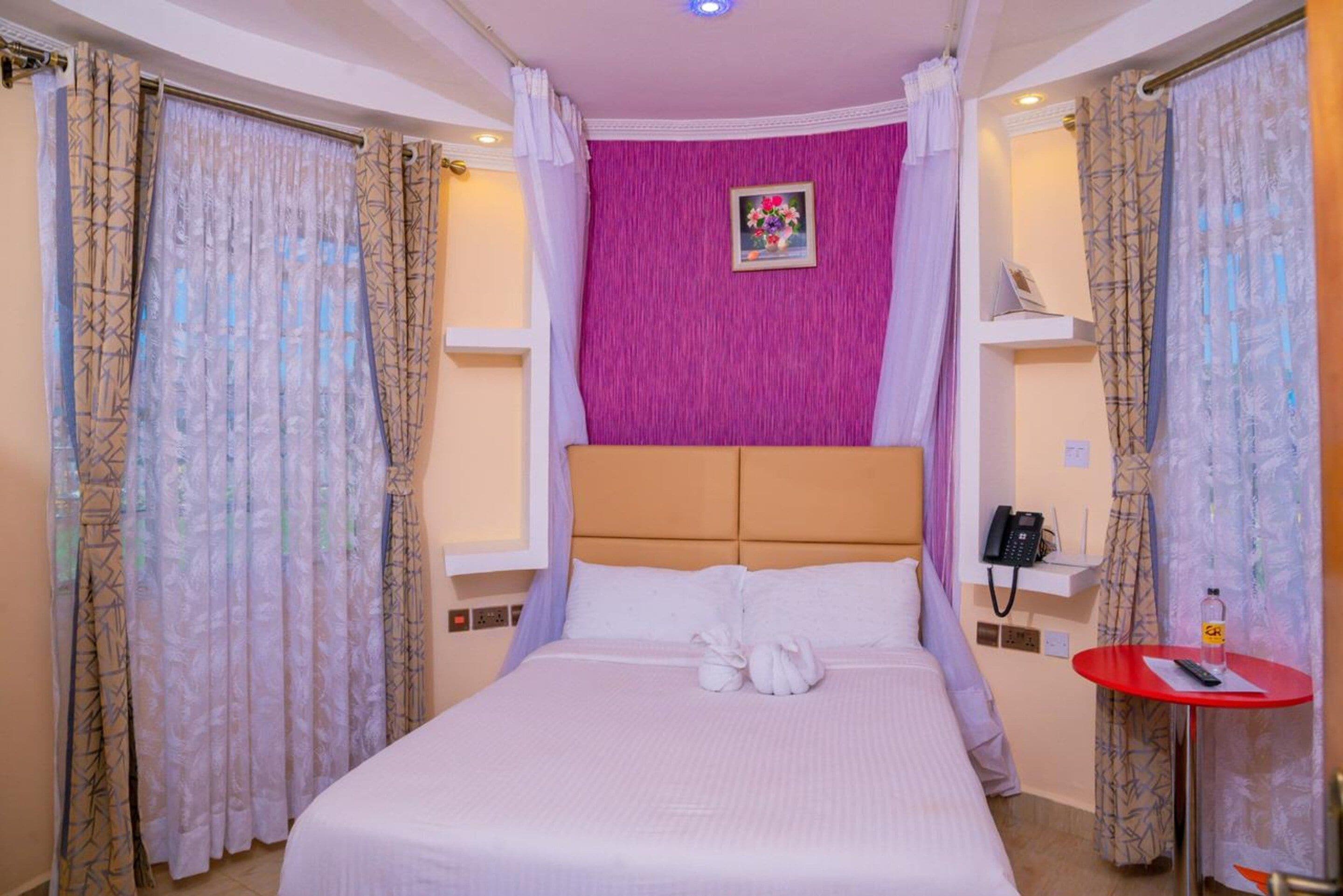 Une chambre d’hôtel avec un lit, une table rouge, un téléphone et un tableau accroché au mur.