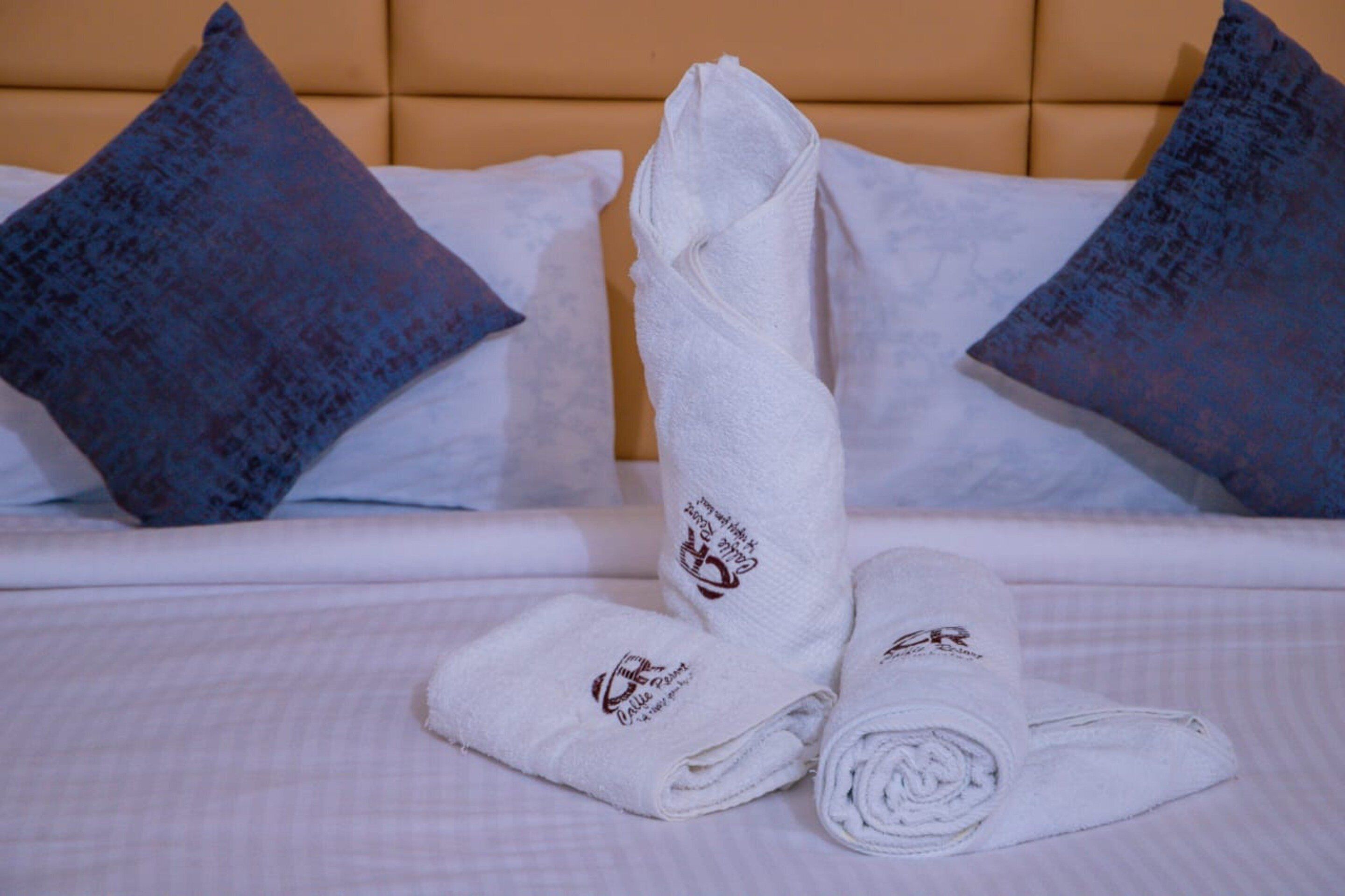 Una cama bien hecha con una toalla doblada y dos almohadas decorativas.