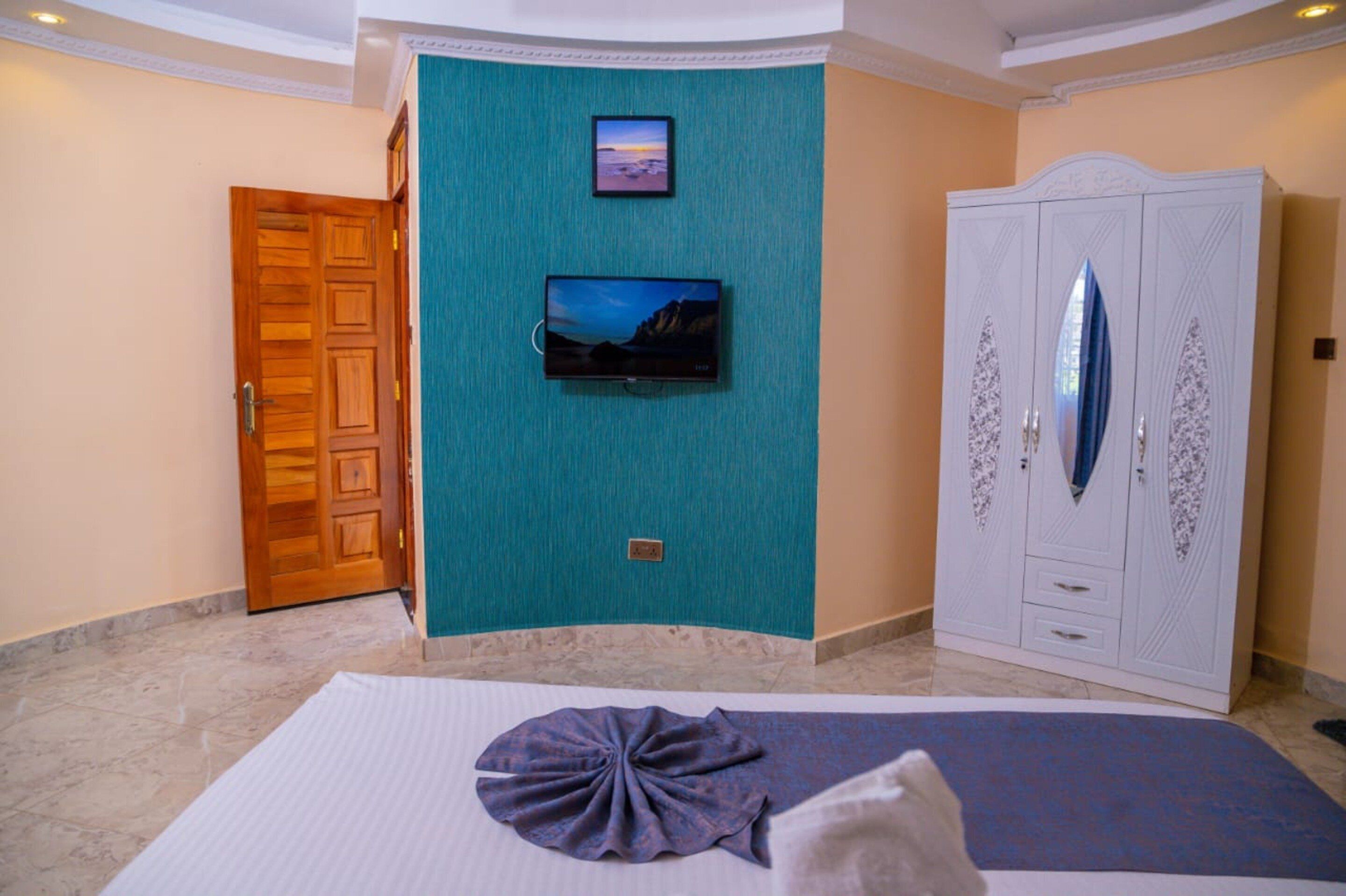 A hotel room with a bed, a television mounted on the wall, a wardrobe, and a door.