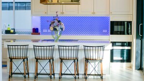 Una cocina moderna con armarios blancos, un salpicadero azul y una isla central con tres sillas negras de metal.
