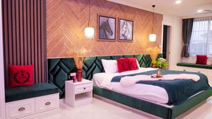 Un dormitorio moderno con una pared de madera en patrón chevron, dos lámparas colgantes, una cama con cabecera tapizada en verde, ropa de cama blanca y una mesita de noche con un florero.