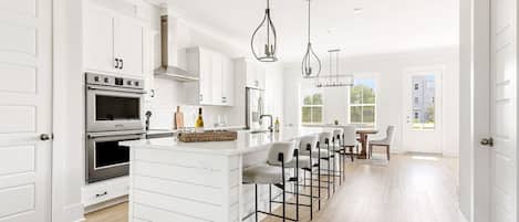 A modern kitchen with white cabinetry, a central island with bar stools, stainless steel appliances, and pendant lighting.