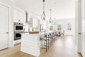Una cocina moderna con armarios blancos, una isla central con taburetes de bar, electrodomésticos de acero inoxidable e iluminación colgante.